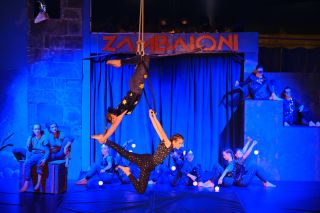 Zwei Artistinnen sind mit einem akrobatischen Kunststück am Ring in der Luft zu sehen.